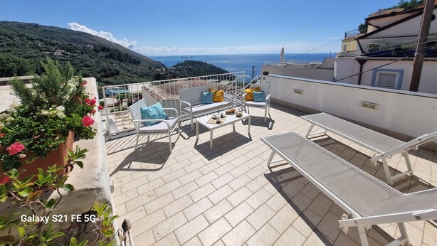 Eine Dachterrasse mit Außenmöbeln, Blick auf das Meer und einem Bergpanorama.