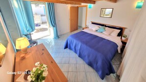 Ein Schlafzimmer mit einem Bett, Holzboden, einem Tisch mit Lampe und einem Fenster mit Vorhängen.
