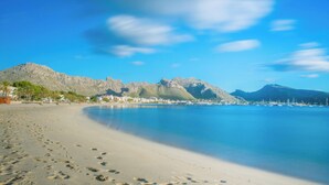 En strand med fodspor, der fører ned til vandet, en klar himmel og bjerge i baggrunden.