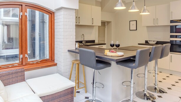 Een moderne keuken met een centraal kookeiland, barkrukken en een zithoek met een bank en een rieten stoel.