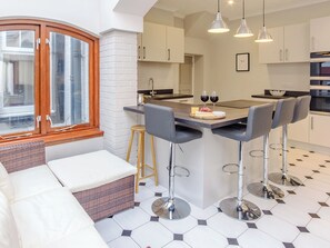 Een moderne keuken met een centraal kookeiland, barkrukken en een zithoek met een bank en een rieten stoel.