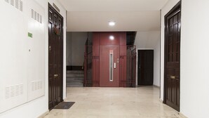 A hallway with lockers on the left, a red door at the end, and a staircase to the right.