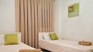 Ein Hotelzimmer mit zwei Einzelbetten, beiger Bettwäsche, grünen Kissen und einem 'LOVE'-Schild an der Wand.