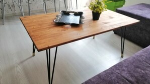 Ein Holztisch mit Tablett und Blumentopf, umgeben von Stühlen und einer Couch in einem modernen Wohnraum.