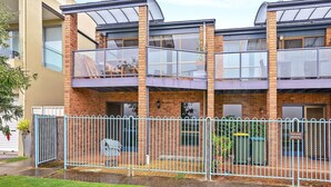 A two-story residential building with a brick facade, large windows, and a metal fence.