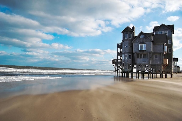 A coastal building with multiple levels and balconies, situated on stilts over the beach.