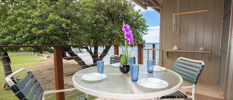 A round table with chairs, a vase with flowers, and a view of the sea.