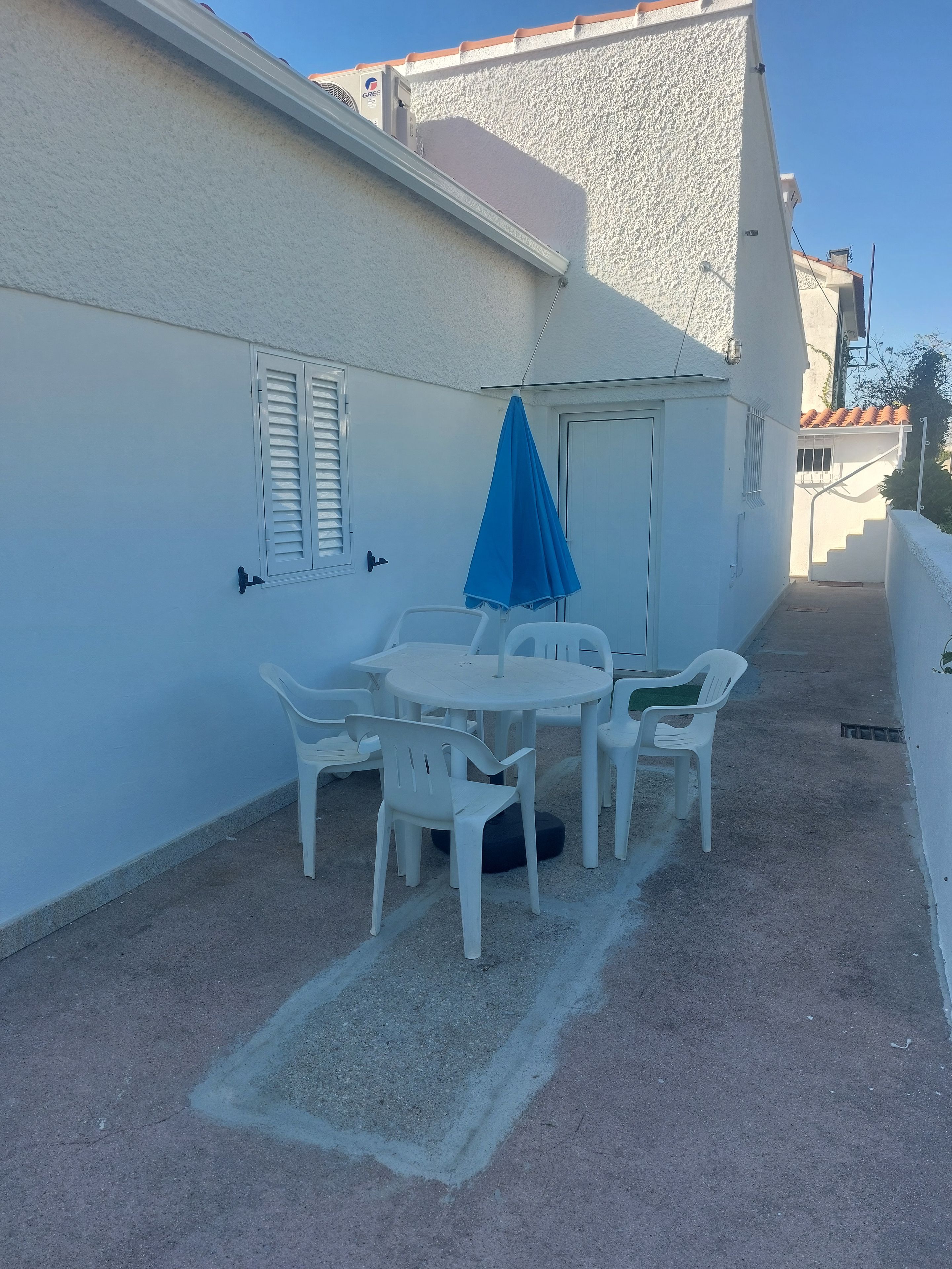 Un pequeño patio al aire libre con una mesa redonda y sillas, un paraguas azul y una pared blanca.