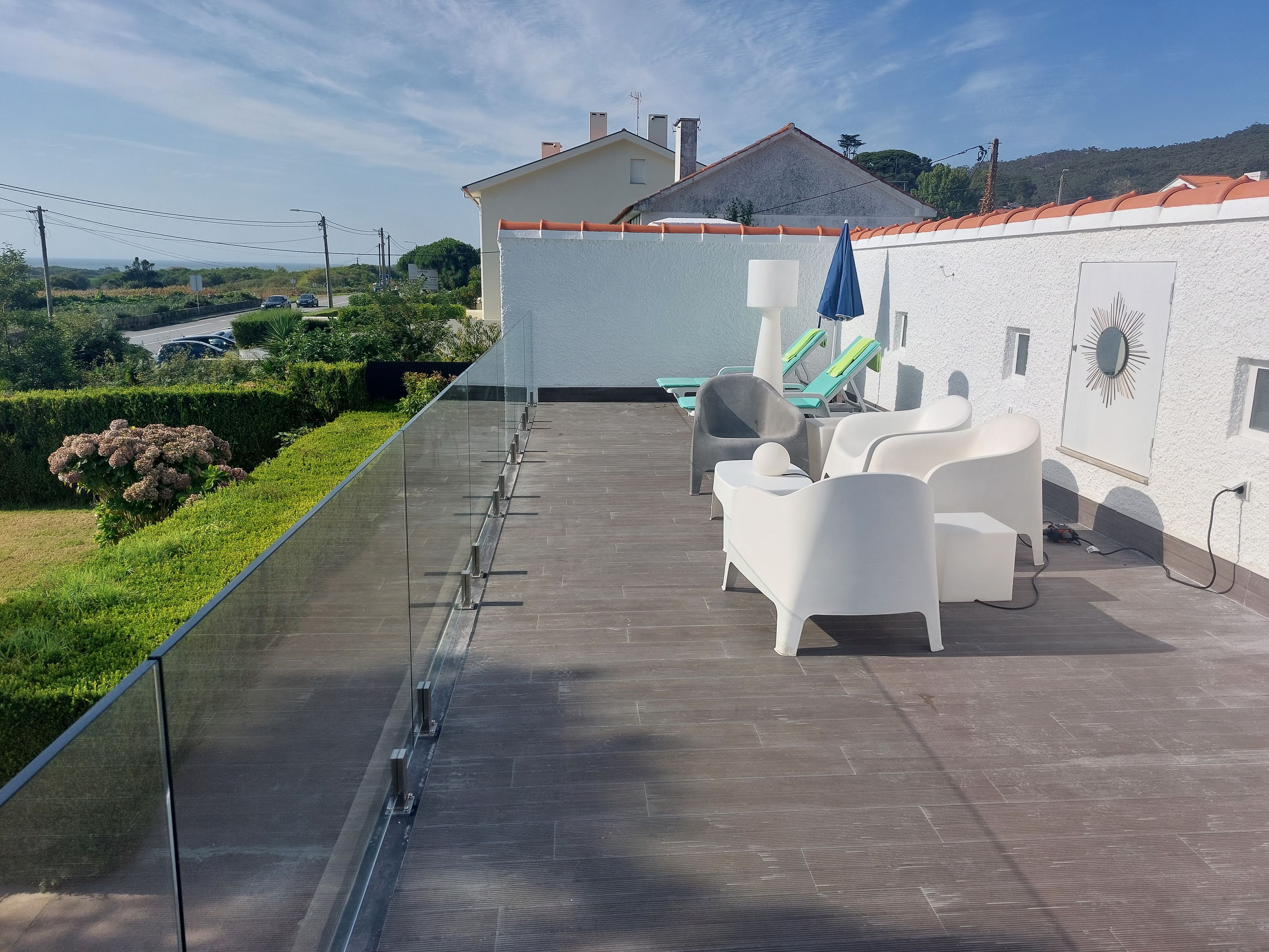 Une terrasse sur le toit dotée d’une balustrade en verre transparent, de chaises longues blanches et offrant une vue sur le paysage environnant.