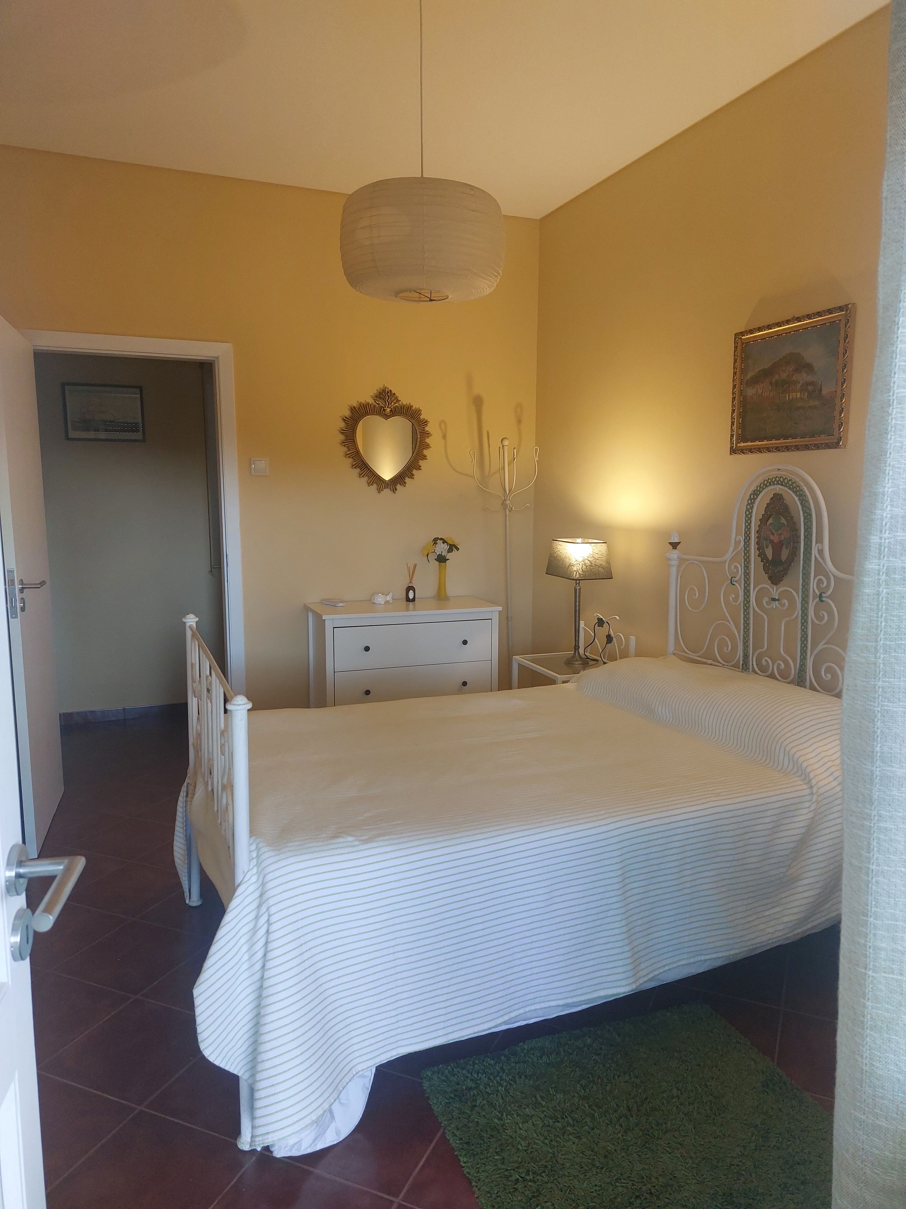 Un dormitorio con una cama, una mesita de noche, una lámpara, un espejo y una puerta.