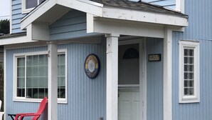 A two-story building with a blue exterior and white trim. There is a red plastic chair outside, a door with a number plate, and a small porch area.