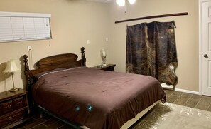 Une chambre à coucher avec un lit en bois, une lampe de chevet, une table de chevet, une fenêtre avec des stores, un rideau et une porte.