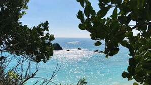 Un sendero que lleva a una playa con aguas azules cristalinas y afloramientos rocosos.