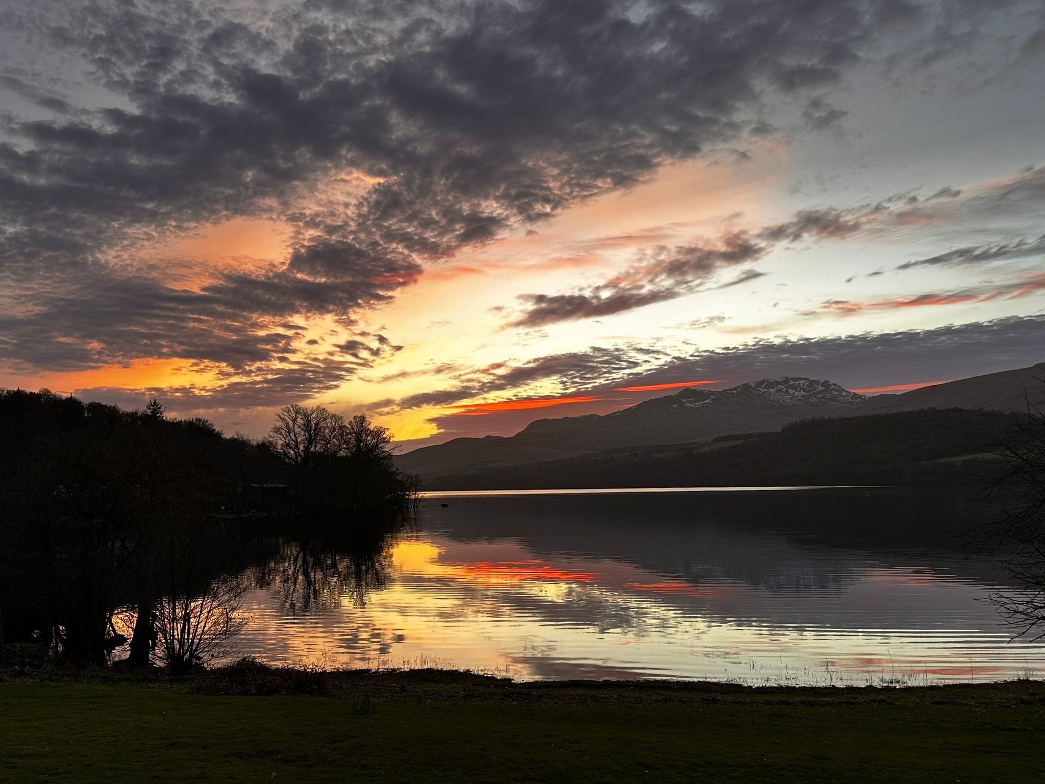 Une vue paisible sur un lac, avec des montagnes en arrière-plan et un ciel nuageux.