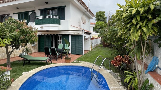 A two-story house with a swimming pool, green shutters, and a balcony.