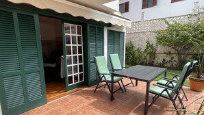 A patio with a table and chairs, a door with green shutters, and a potted plant.