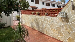 A courtyard with a stone wall, tiled floor, and potted plants.
