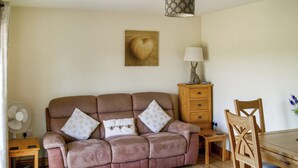 A living room with a sofa, a wooden cabinet, a table, and a chair. - The Stables at Greenview (Winsham, near Chard)