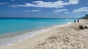 A beach with clear turquoise water, a sandy shore, and a few people walking. - Newly Renovated Ocean View White Sand Beachfront 3 Bed 3 Bath Two Level Condo (Cancún)