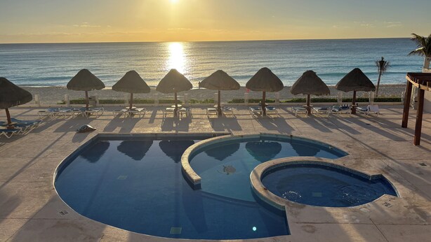 A pool area with sun loungers and umbrellas, overlooking the ocean. - Newly Renovated Ocean View White Sand Beachfront 3 Bed 3 Bath Two Level Condo (Cancún)