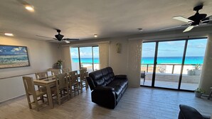 A spacious living area with a wooden floor, a black leather sofa, a dining table with chairs, and large windows offering a view of the beach. - Newly Renovated Ocean View White Sand Beachfront 3 Bed 3 Bath Two Level Condo (Cancún)