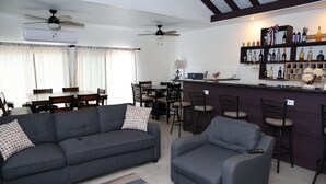 A living room with a sofa, armchair, and a bar area with shelves of bottles. - Cozy Eastern Beachfront Villas (Grand Bahama)
