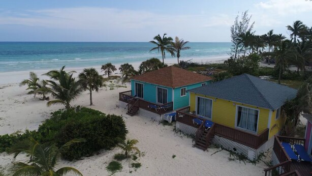 A beachfront property with two colorful houses, one blue and one yellow, featuring balconies and a sandy beach with palm trees. - Cozy Eastern Beachfront Villas (Grand Bahama)