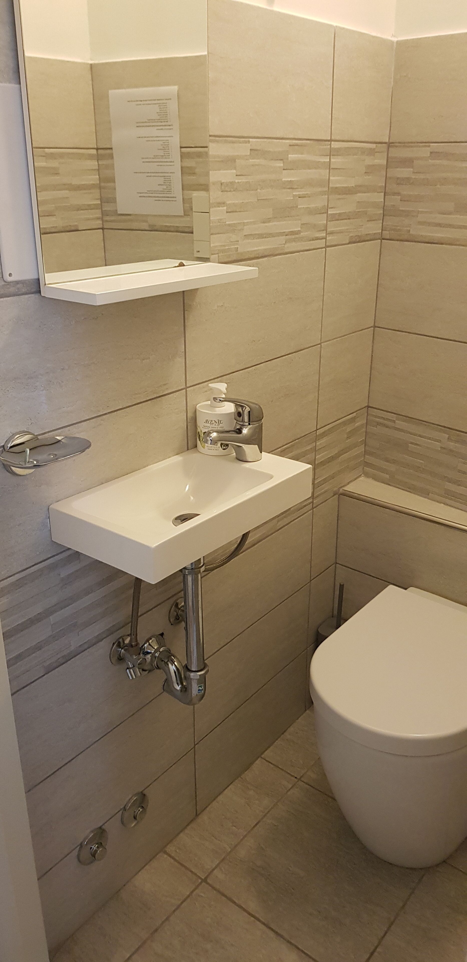 A bathroom with a white sink, a mirror, a toilet, and a paper on the wall.