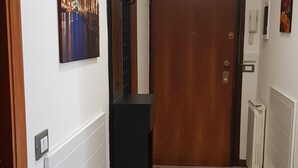 Een gang met een betegelde vloer, een houten deur, een radiator en een aan de muur bevestigde telefoon.