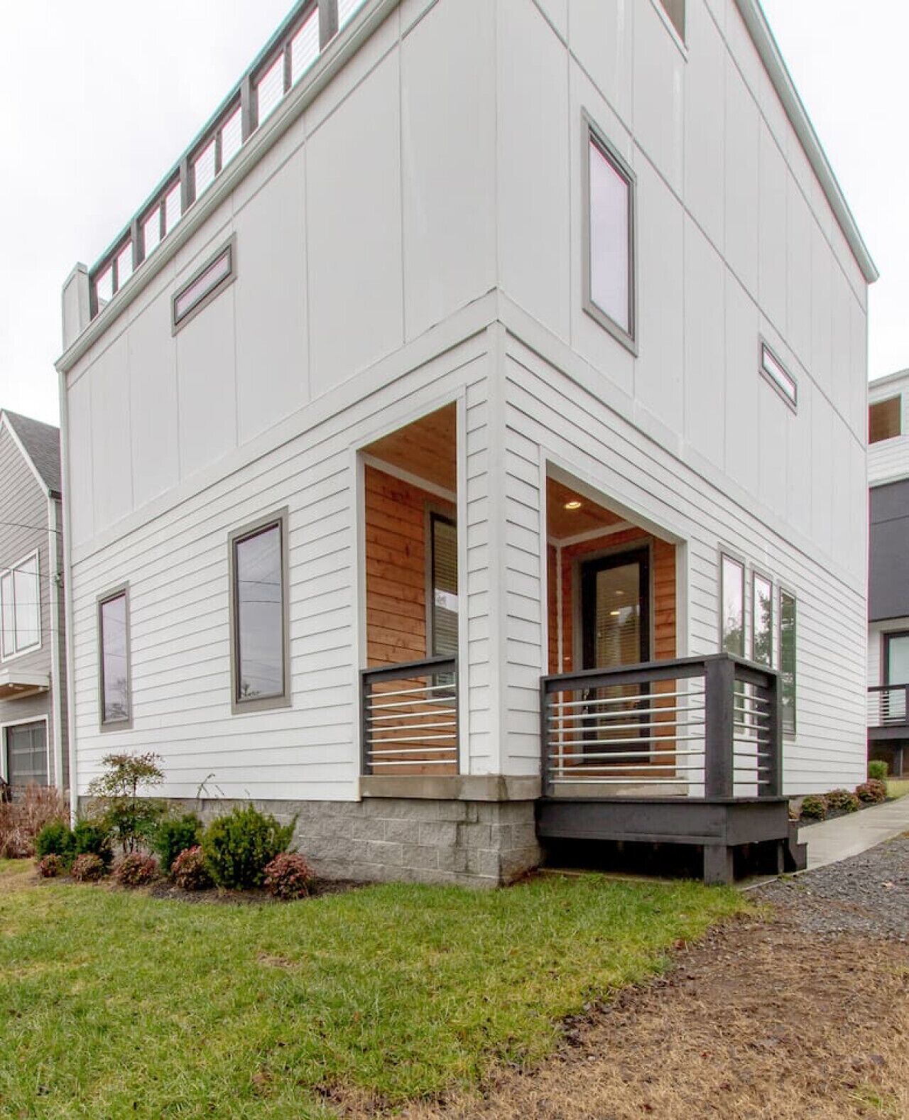 Une maison moderne à deux étages, dotée d’un toit plat, de grandes fenêtres et d’un petit porche avec une balustrade.