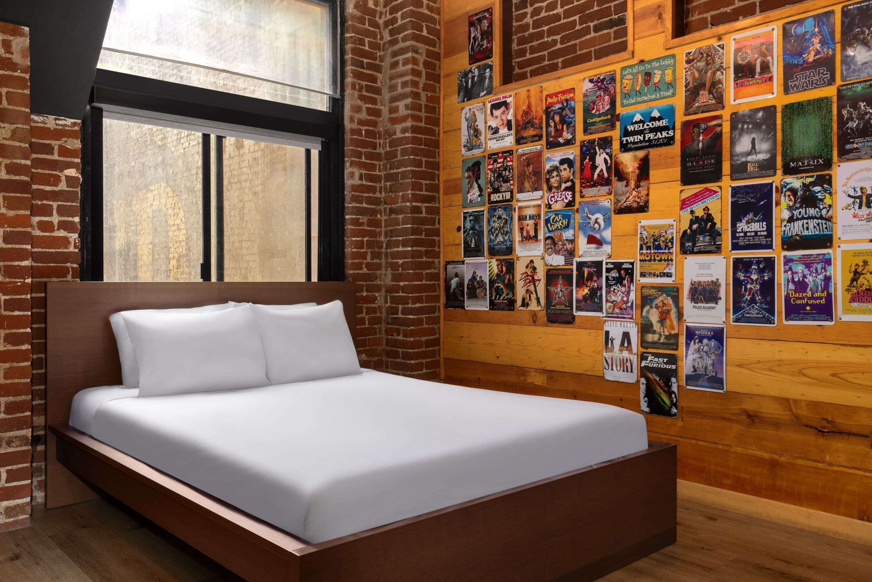 Un dormitorio moderno con una cama de madera, paredes de ladrillo y una pared llena de carteles de películas.