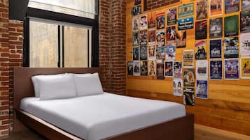 Un dormitorio moderno con una cama de madera, paredes de ladrillo y una pared llena de carteles de películas.