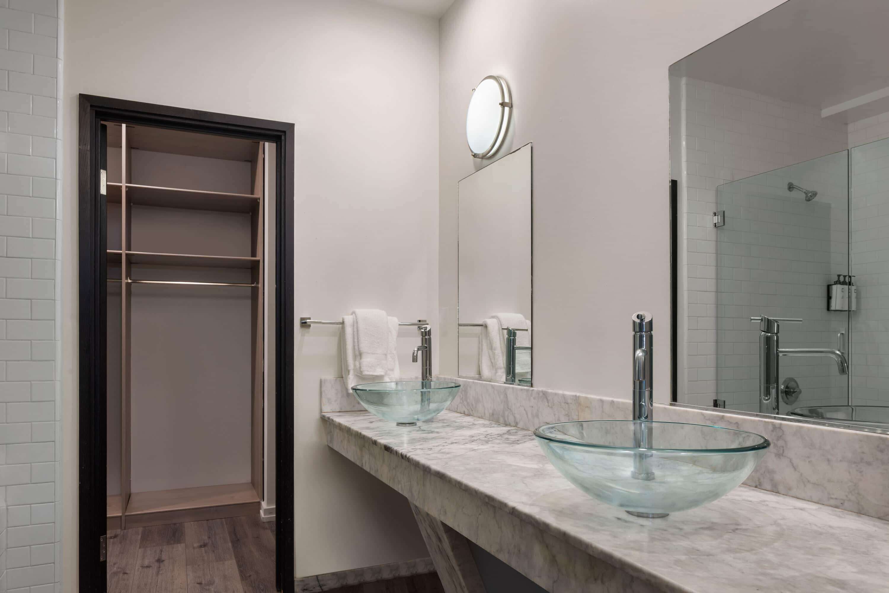 A modern bathroom with a glass bowl sink, a large mirror, and a walk-in shower.
