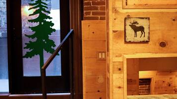Interior de madera con una ventana que muestra la silueta de un árbol, una puerta de madera y un cartel con la imagen de un alce.