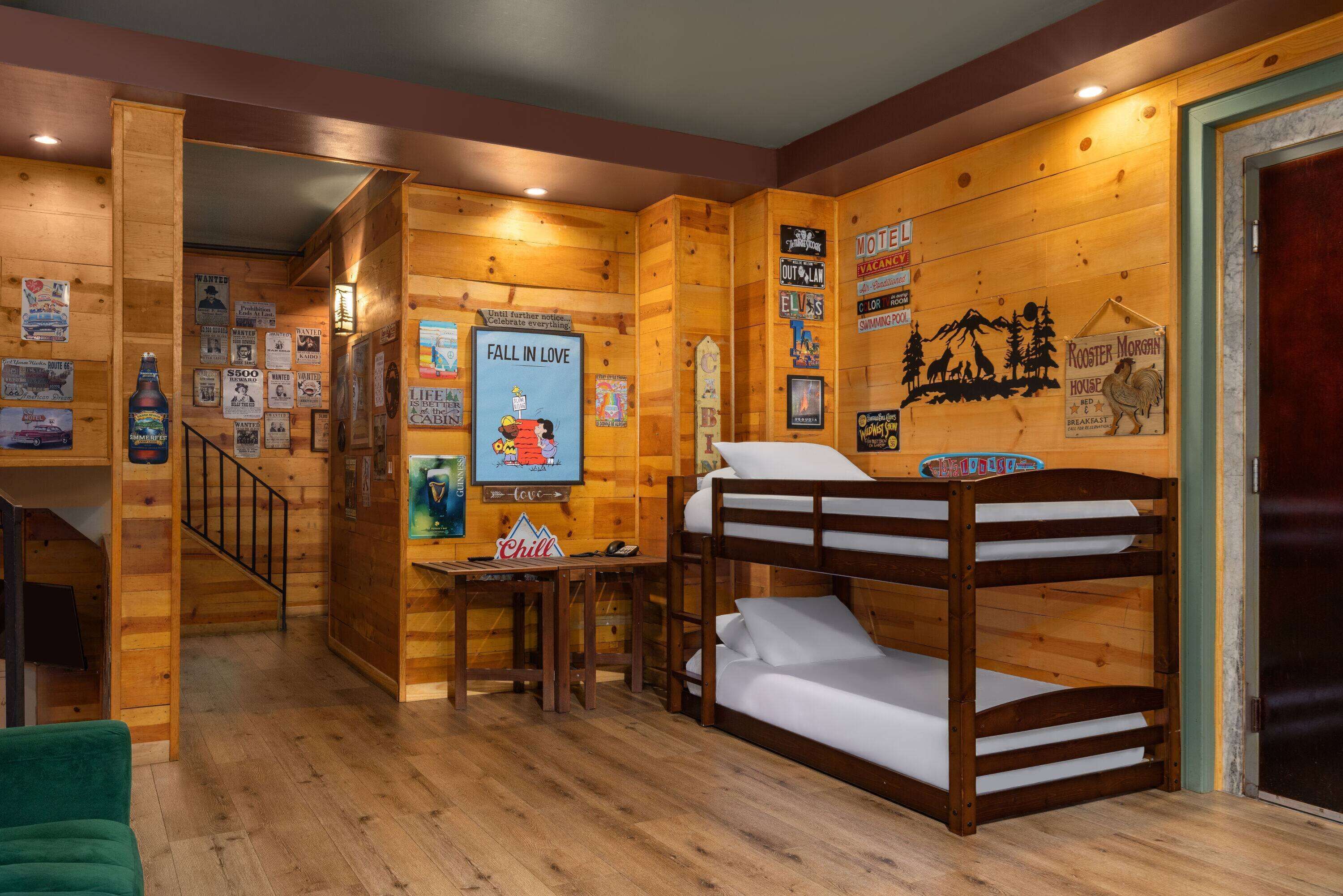 Una habitación acogedora tipo cabaña, con paredes de madera, una litera, una mesita pequeña y varios carteles y letreros.
