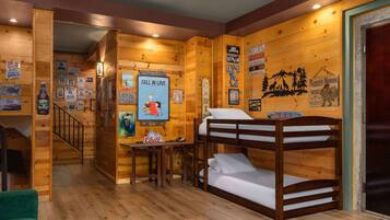 Una habitación acogedora tipo cabaña, con paredes de madera, una litera, una mesita pequeña y varios carteles y letreros.