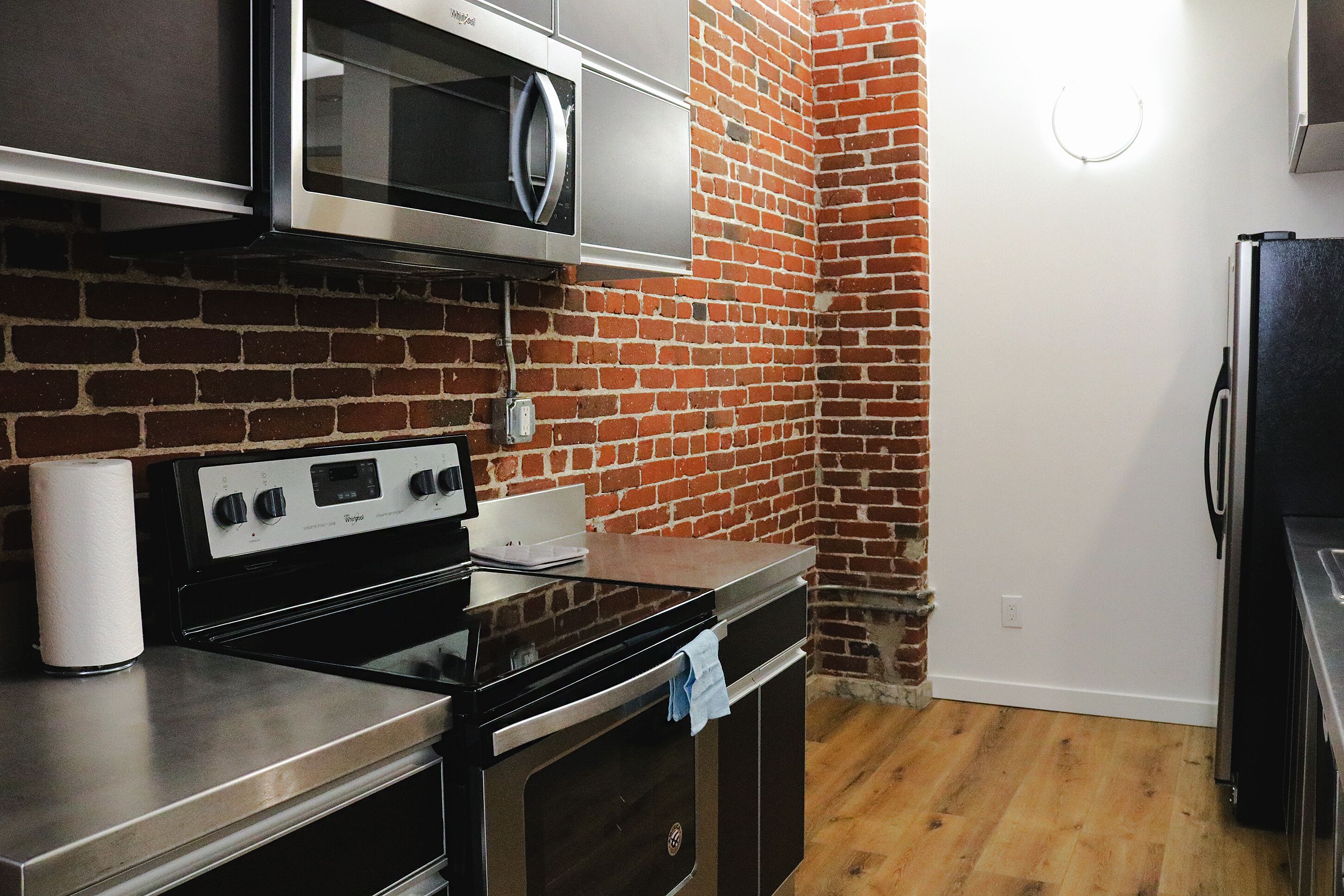 A kitchen with a brick wall, stainless steel appliances, and wooden flooring.
