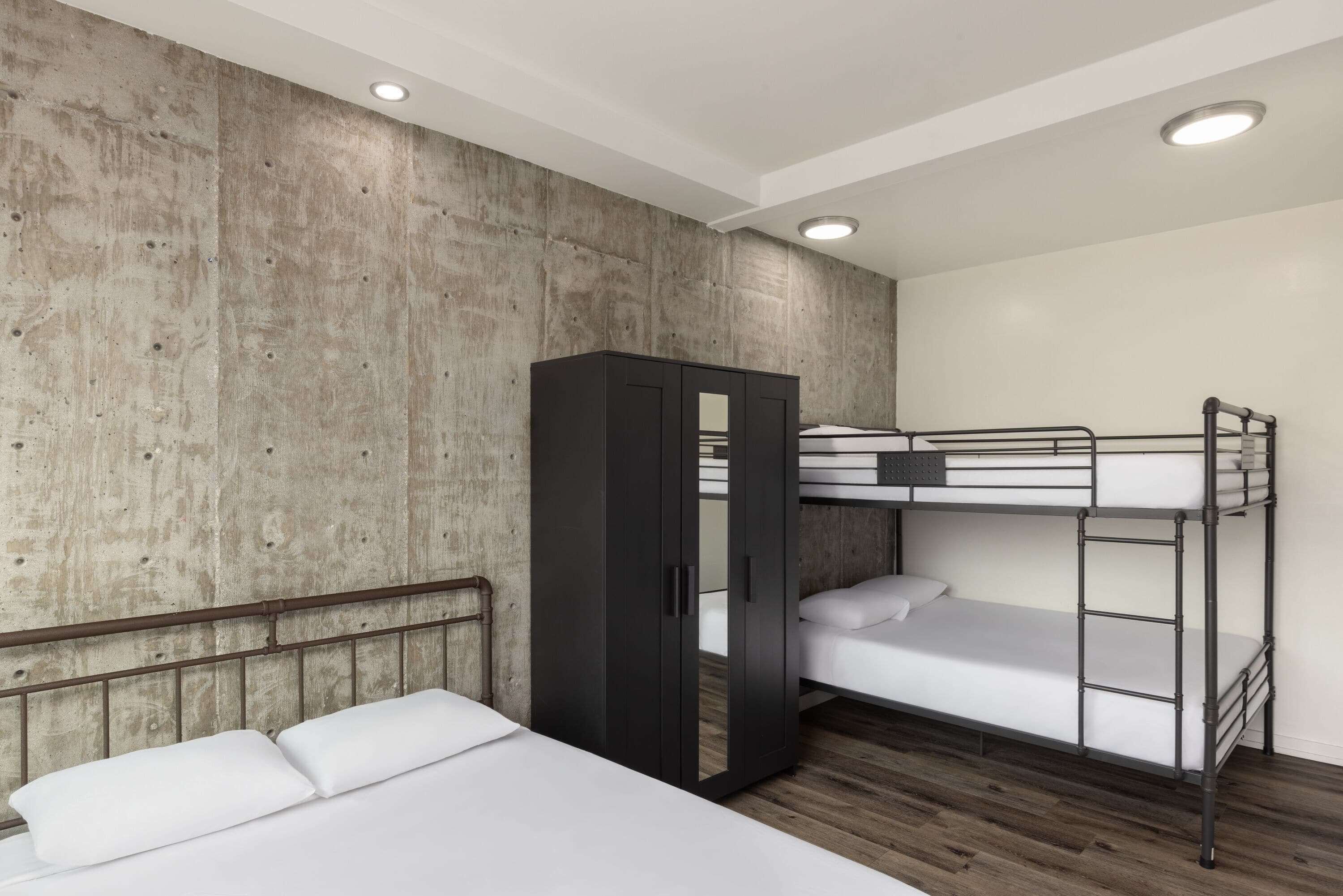 A bunk bed room with a wooden headboard, a wardrobe, and a concrete wall.