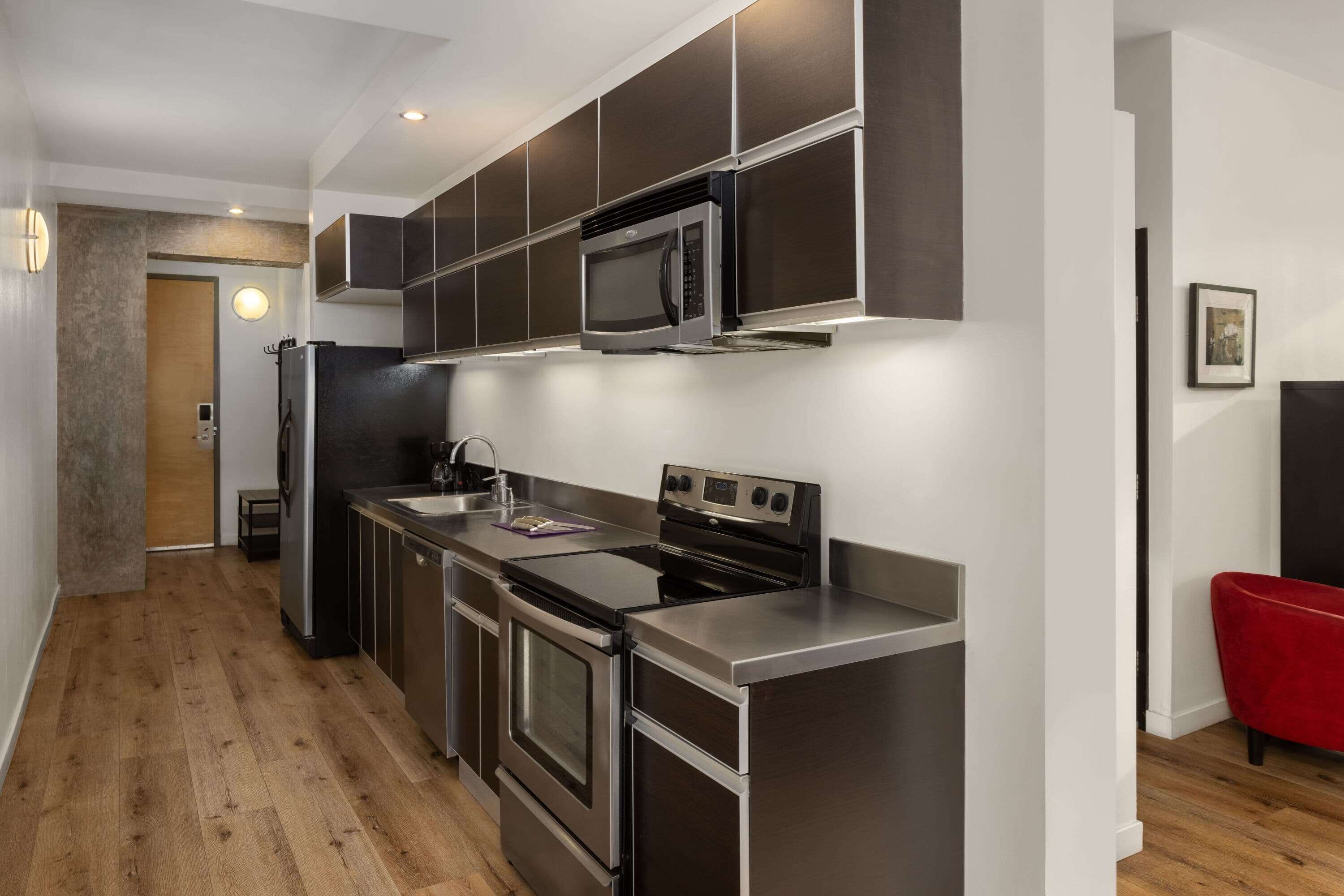 Una cocina moderna con electrodomésticos de acero inoxidable, piso de madera y una silla roja.