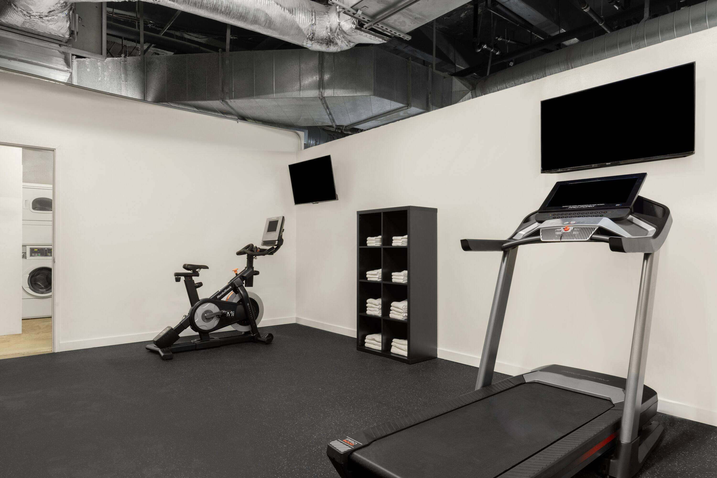 Une salle de sport équipée d’un tapis de course, d’un vélo d’appartement et d’un téléviseur fixé au mur.