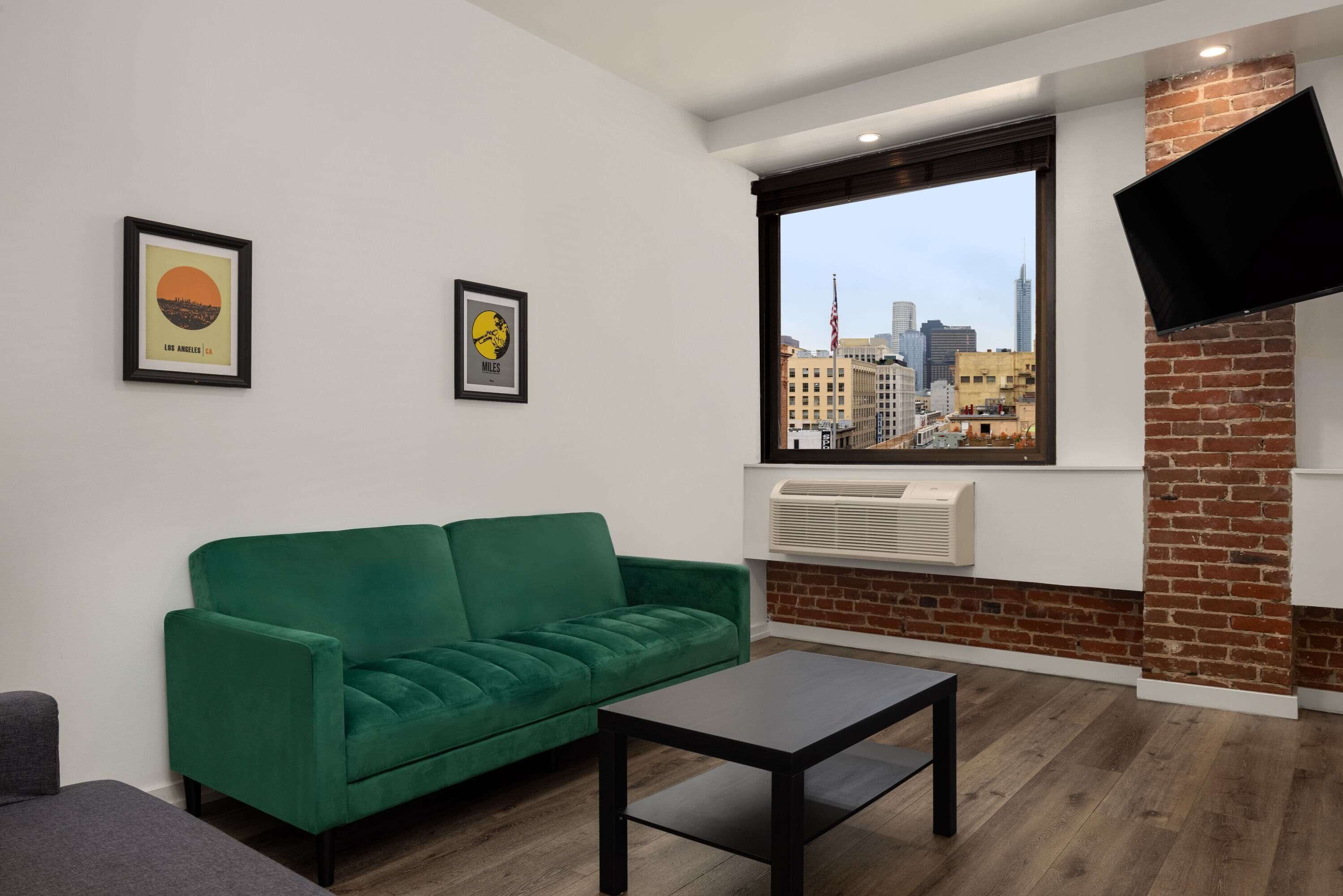 Un salon moderne avec un canapé vert, une table basse noire et une grande fenêtre donnant sur la ville.
