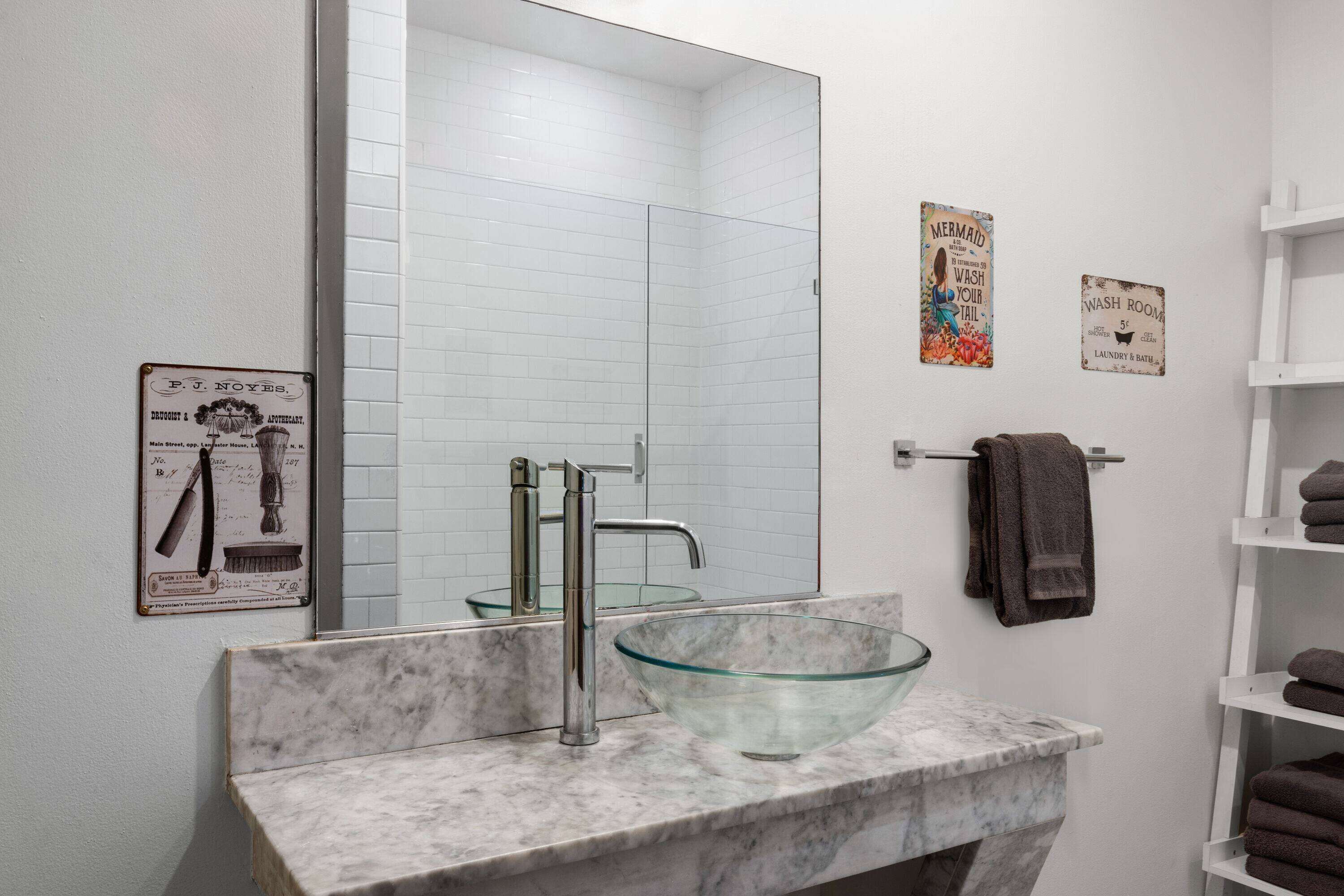 Une salle de bain avec un lavabo en verre en forme de bol, un grand miroir et un porte-serviettes.
