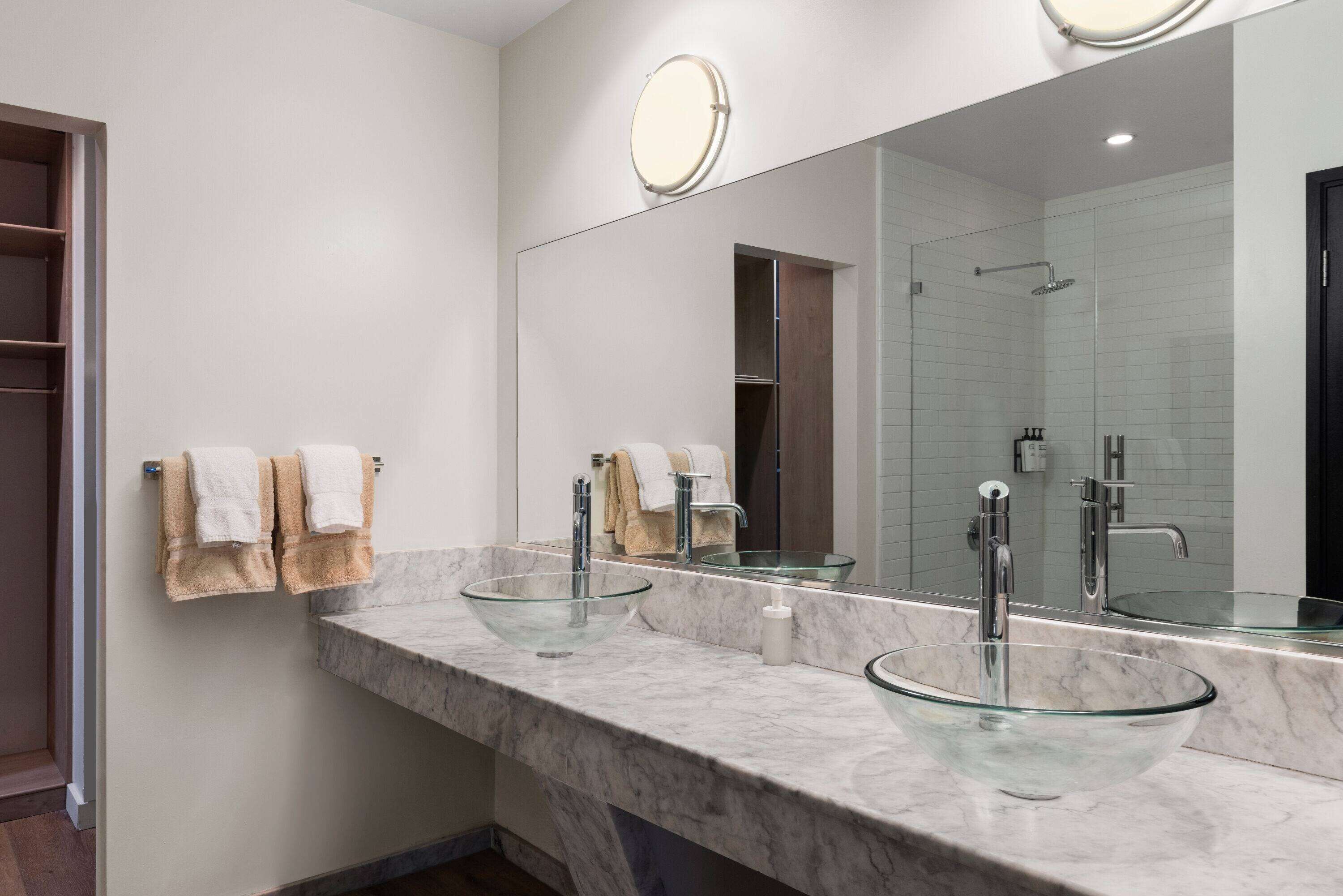 Ein modernes Badezimmer mit zwei Glaswaschbecken, einem großen Spiegel und einer bodengleichen Dusche.