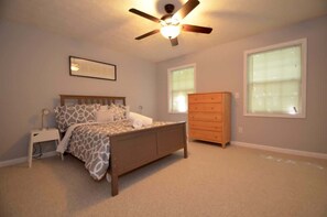 A bedroom with a bed, nightstand, dresser, ceiling fan, and two windows.