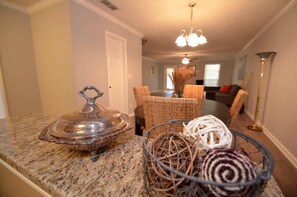 A kitchen with granite countertops, a dining area with wicker chairs, and a chandelier.