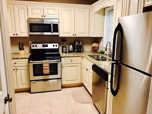A kitchen with white cabinetry, a stainless steel refrigerator, a microwave, an oven, and a dishwasher.