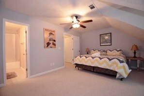 A bedroom with a bed, a ceiling fan, a door, and a poster on the wall.