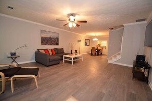 A living room with a grey sofa, a coffee table, a ceiling fan, and a staircase leading to another room.