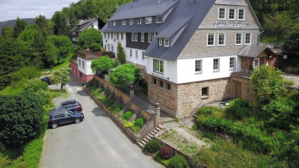 A large, two-story house with a steeply pitched roof, surrounded by lush greenery and trees. - B&B Sauerland TCF (Willingen)