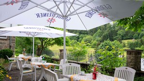 An outdoor seating area with white chairs and tables, covered by large umbrellas with the brand name visible. - B&B Sauerland TCF (Willingen)